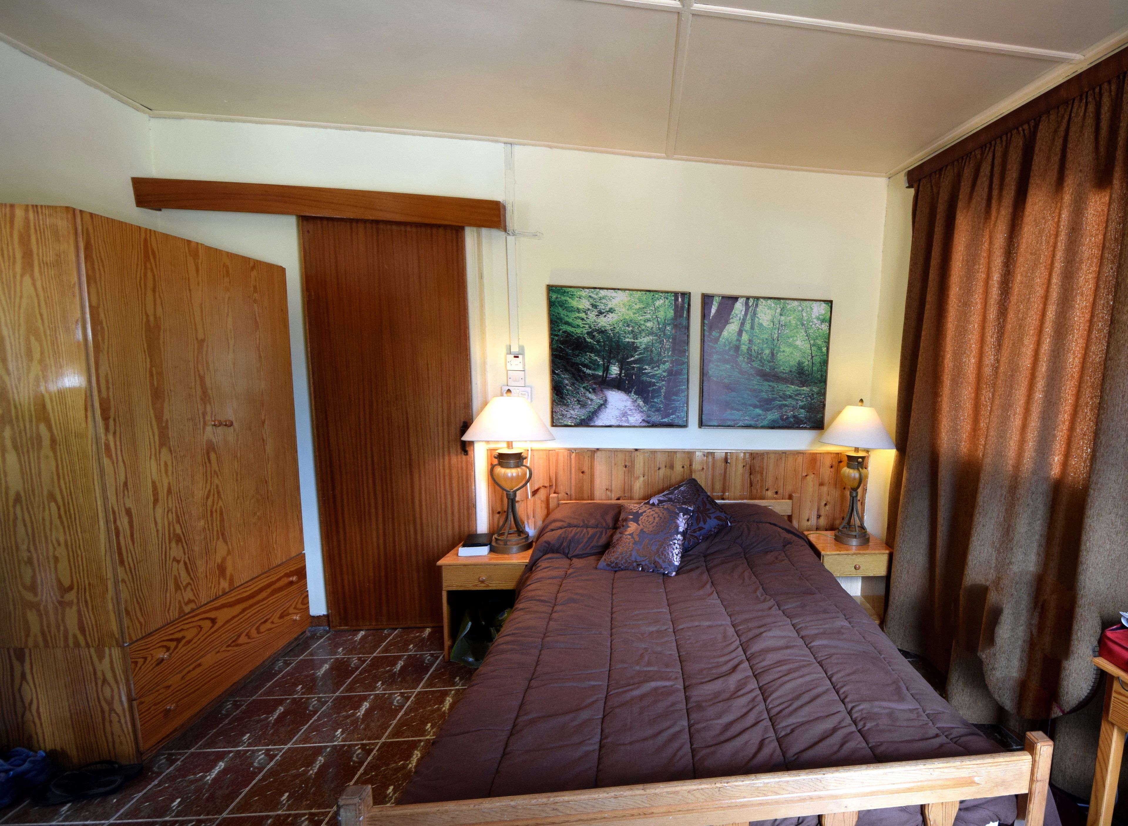 A bedroom with a wooden bed, two bedside lamps, a nightstand, and a wardrobe.