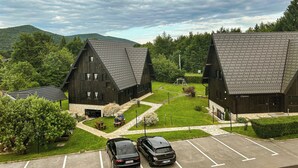 Vista de un estacionamiento con dos coches, un área verde con un columpio y dos edificios de madera grandes con techos empinados.