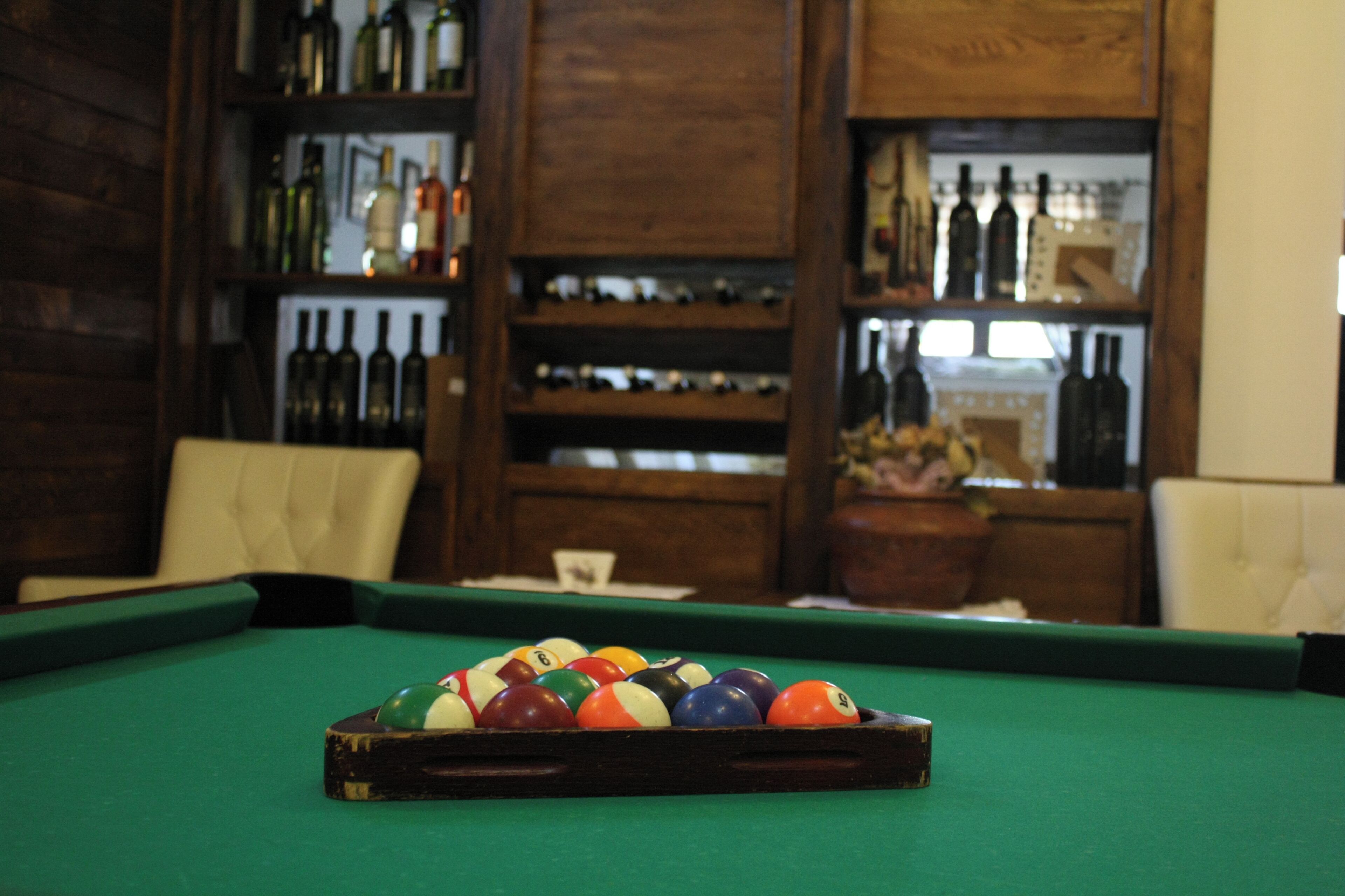 A pool table with balls in a room with wooden shelves containing bottles.