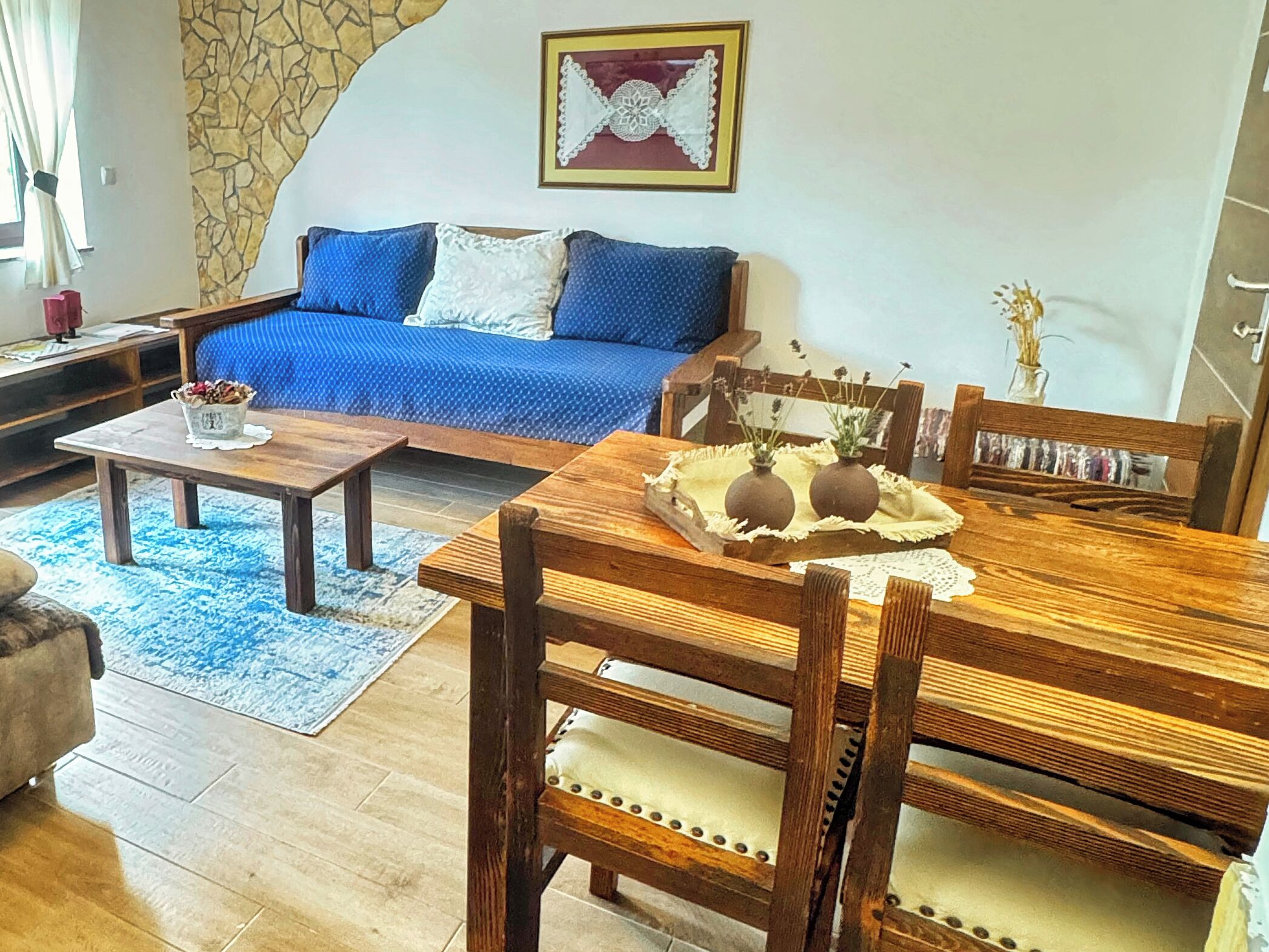 A living room with a blue sofa, wooden dining table, and a stone accent wall.
