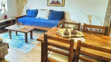 A living room with a blue sofa, wooden dining table, and a stone accent wall.