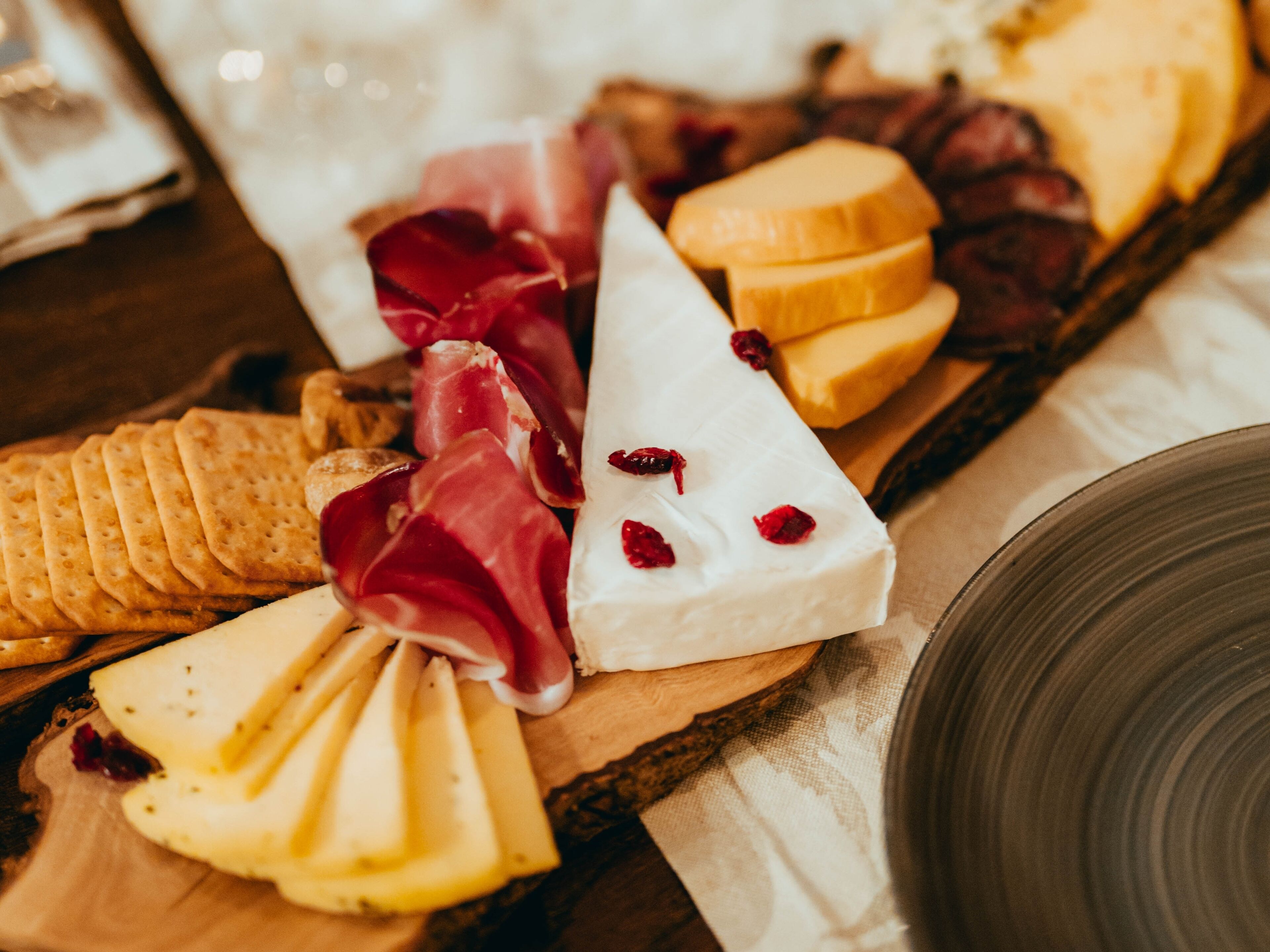A wooden board with various cheeses, crackers, and cured meats.