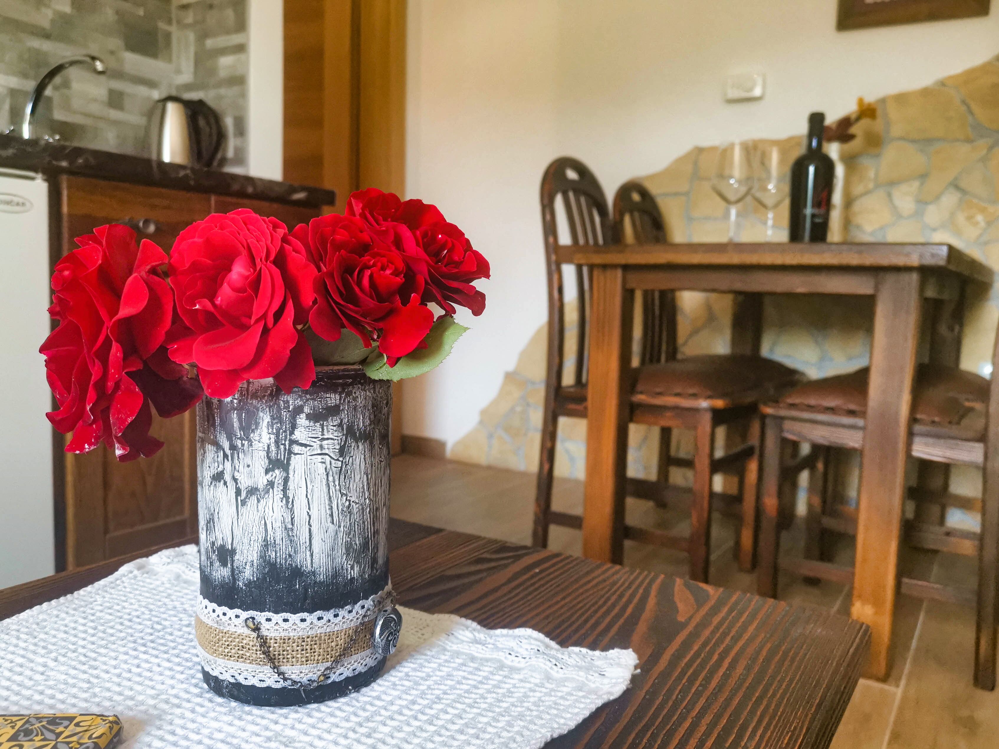 A rustic dining table with a vase of red roses on a textured placemat.