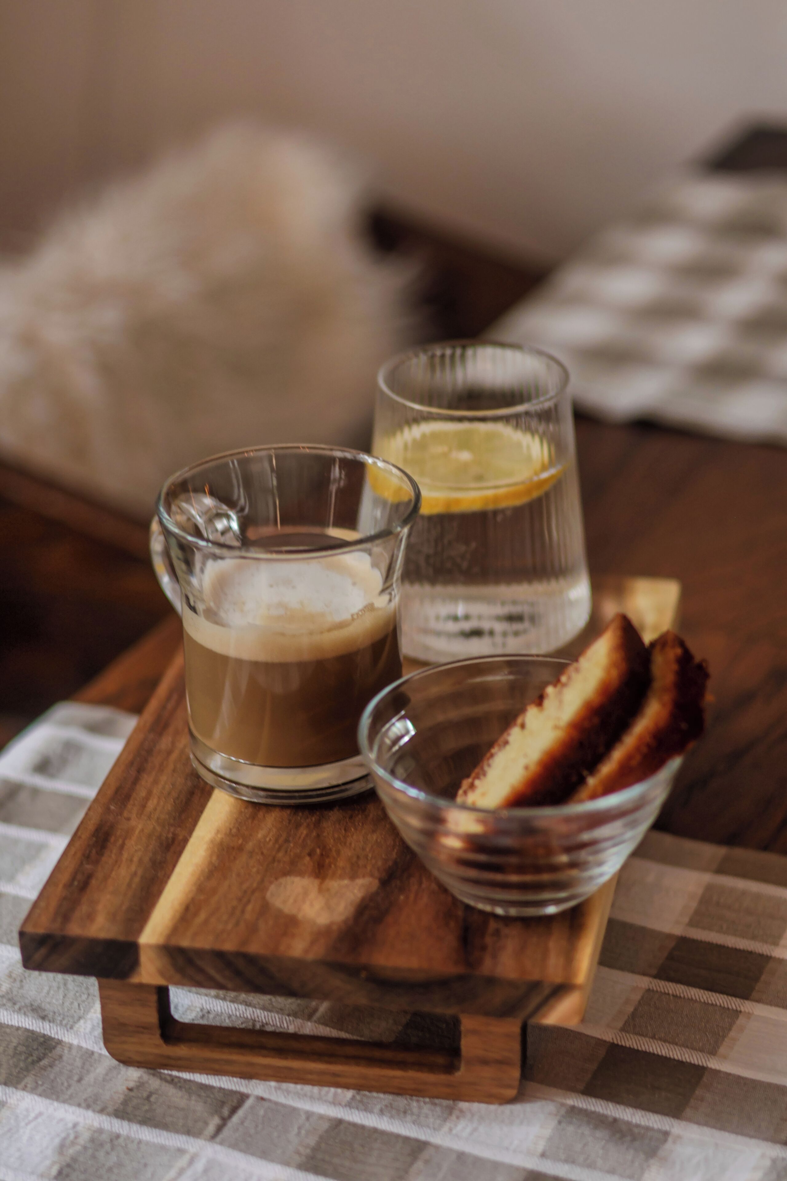 Una bandeja de madera con una taza de café, un vaso de agua y un bol de pan.