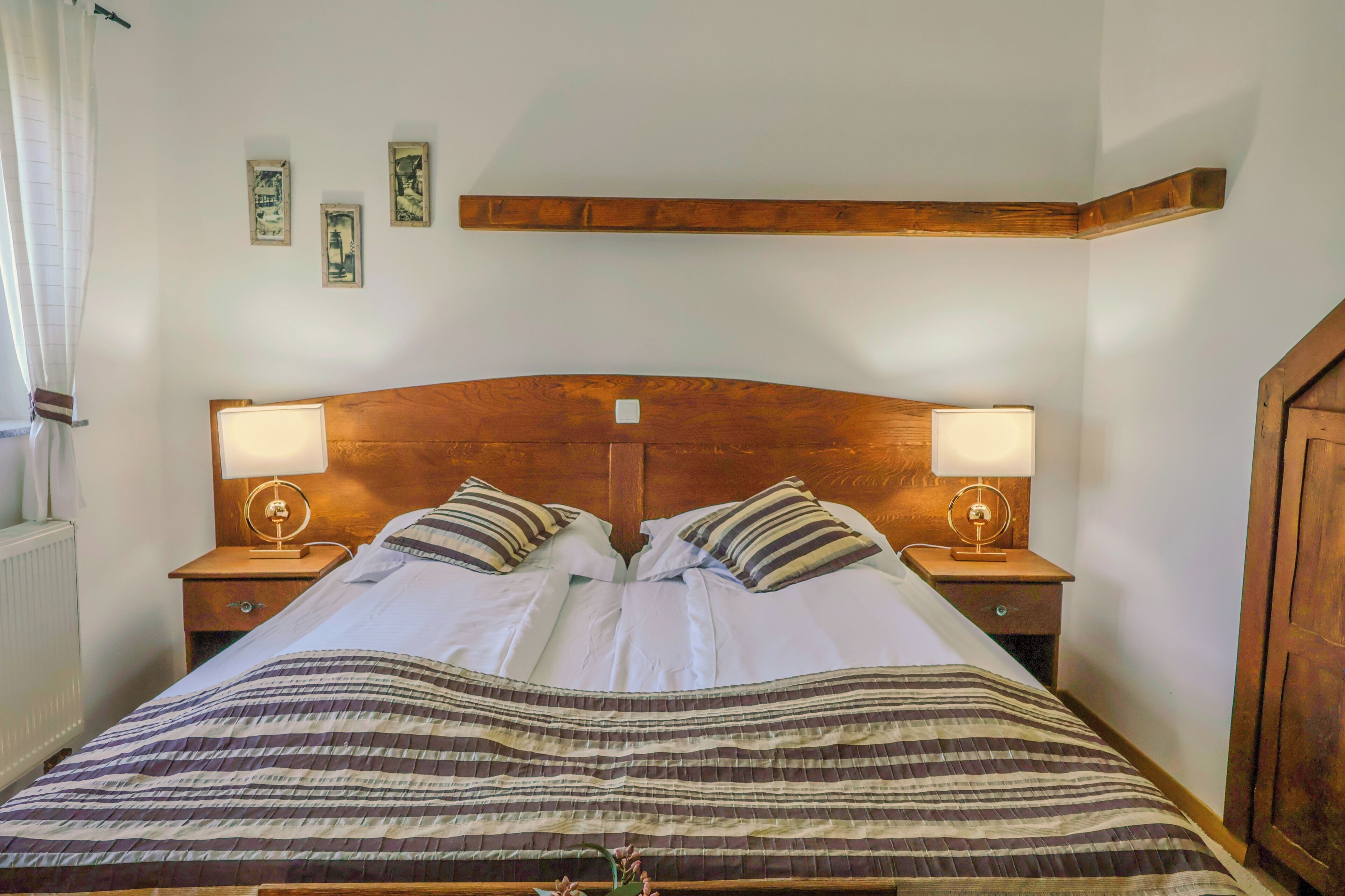 Una cama con cabecera de madera, dos mesitas de noche con lámparas y una ventana con cortinas.