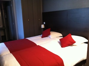 A hotel room with a bed, red and white bedding, a dark headboard, and a nightstand with a lamp.