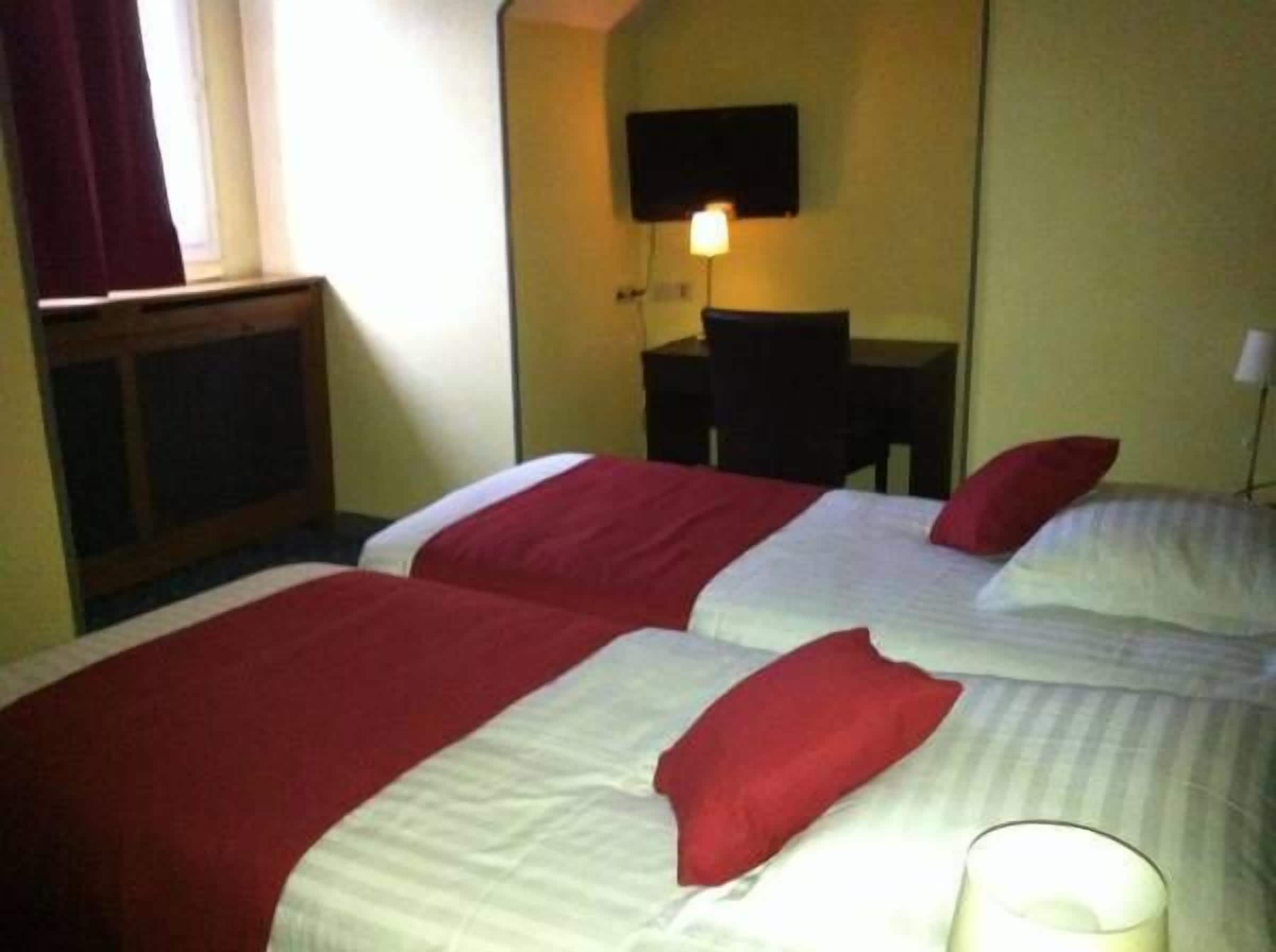 A hotel room with two beds, a desk, a chair, and a TV mounted on the wall.