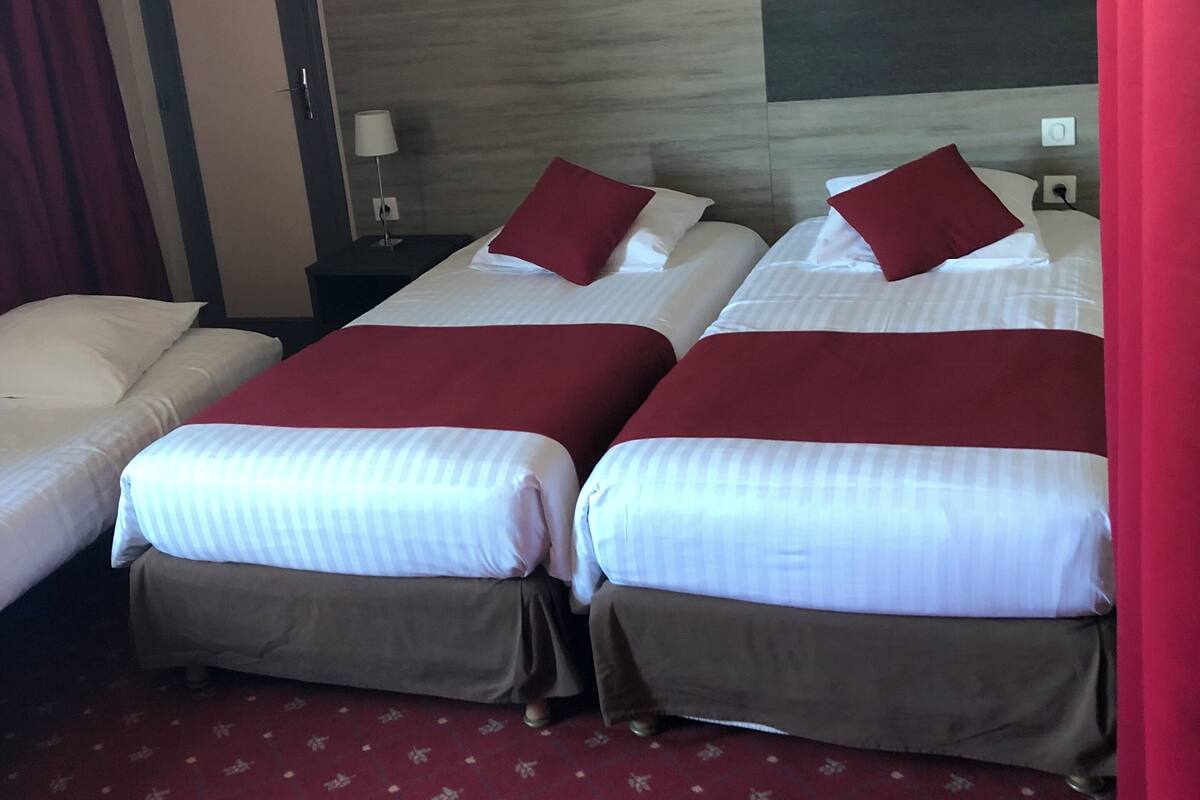Una habitació d'hotel amb dos llits, cada un amb roba de llit blanca i almoinades vermelles, un capçal de llit de fusta i una catifa vermella amb disseny.
