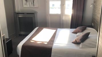 Una habitación de hotel con cama, radiador, puerta y ventana con cortinas.