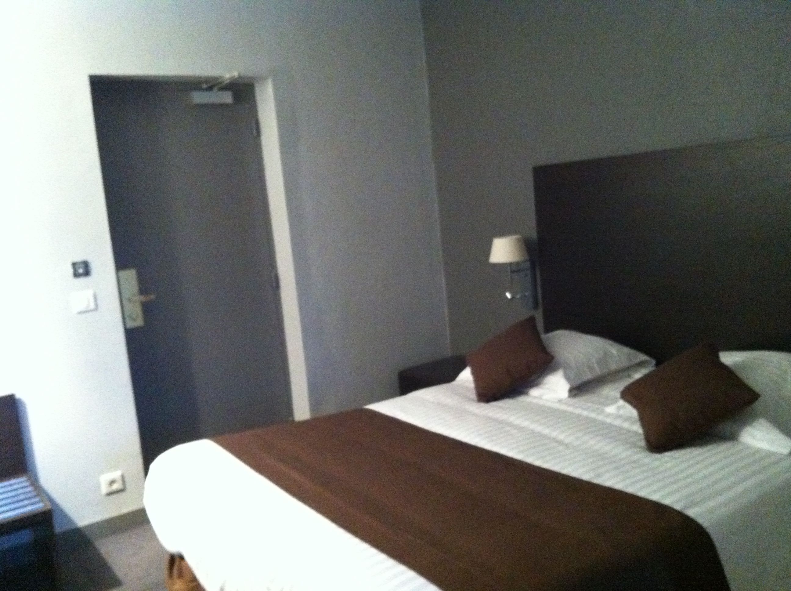 A hotel room with a bed, a nightstand, a lamp, and a door.