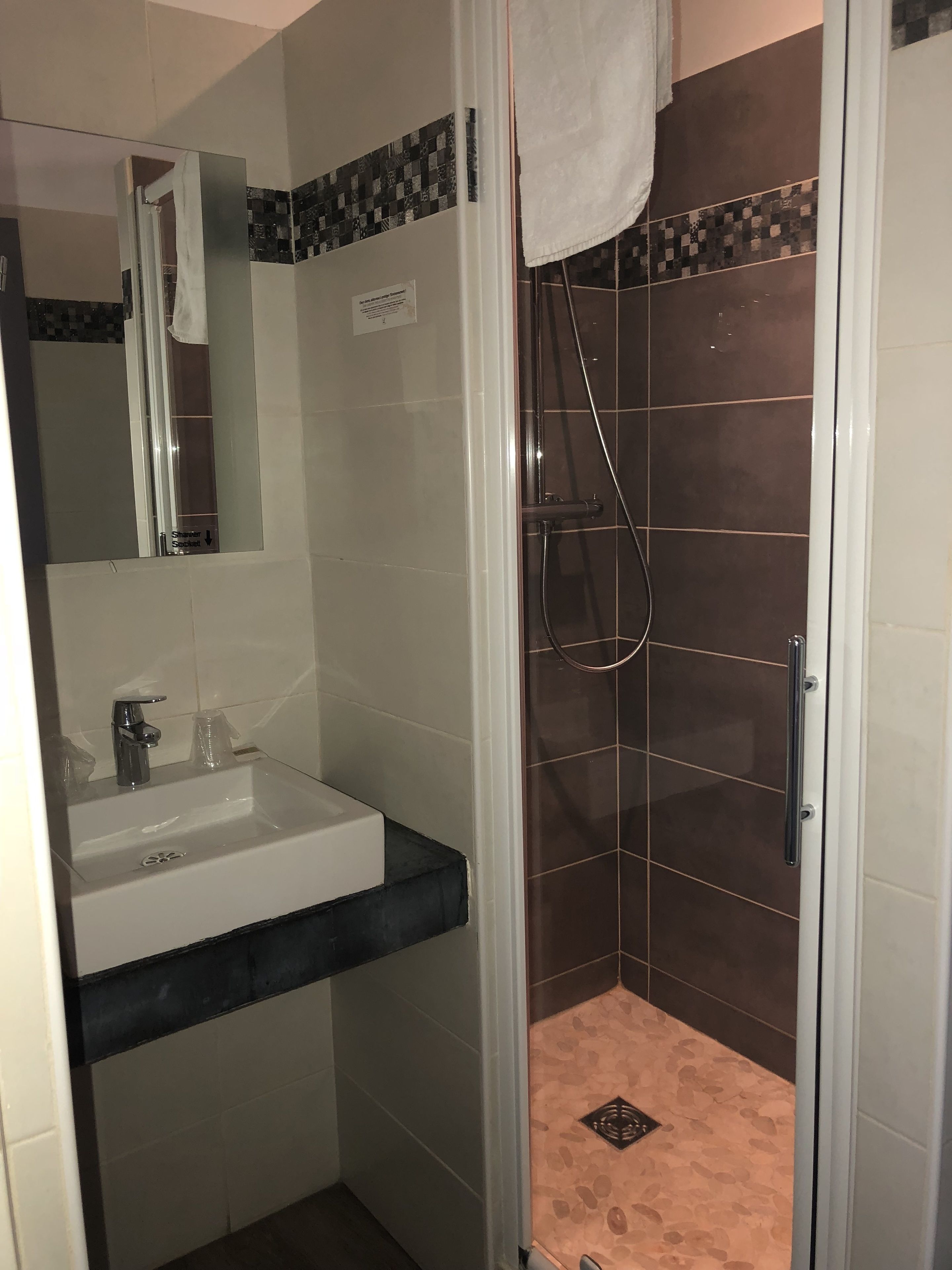 A bathroom with a glass-enclosed shower, a sink with a mirror, and tiled walls.