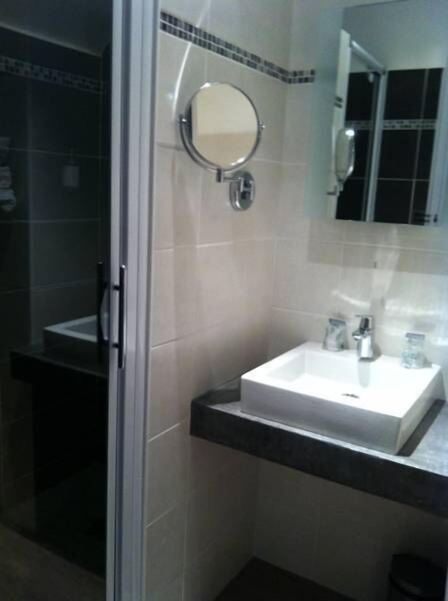 Un baño con lavamanos blanco, espejo y zona de ducha.