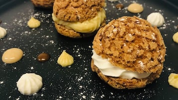 Three dessert items on a dark plate with powdered sugar and small dollops of cream.