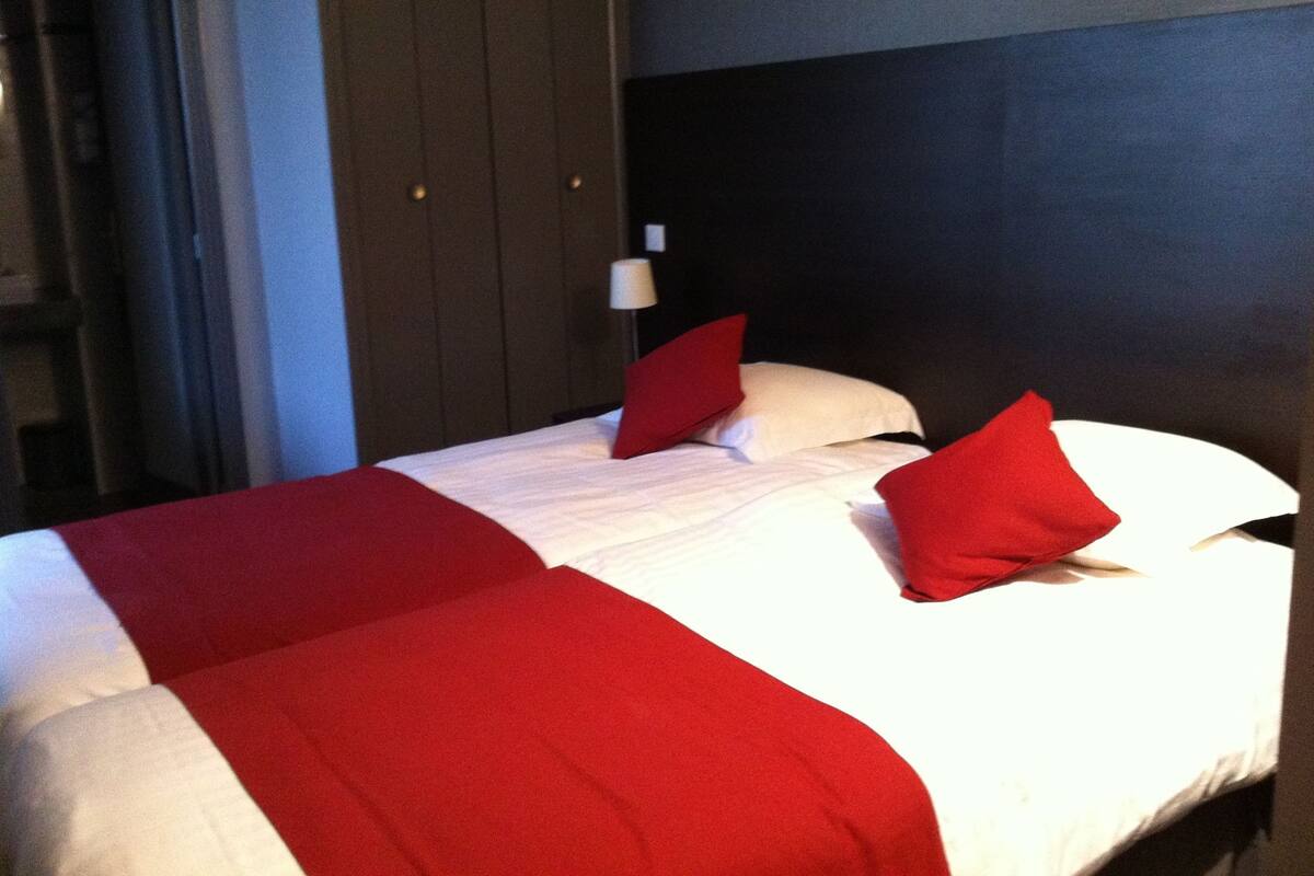 Habitació d'hotel amb llit, roba de llit vermella i blanca, capçaleri fosc i una làmpada penjada a la paret.