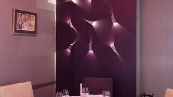 Un coin repas avec une table ronde dressée pour quatre personnes, un mur moderne agrémenté d’un éclairage décoratif abstrait et un tableau encadré accroché au mur.