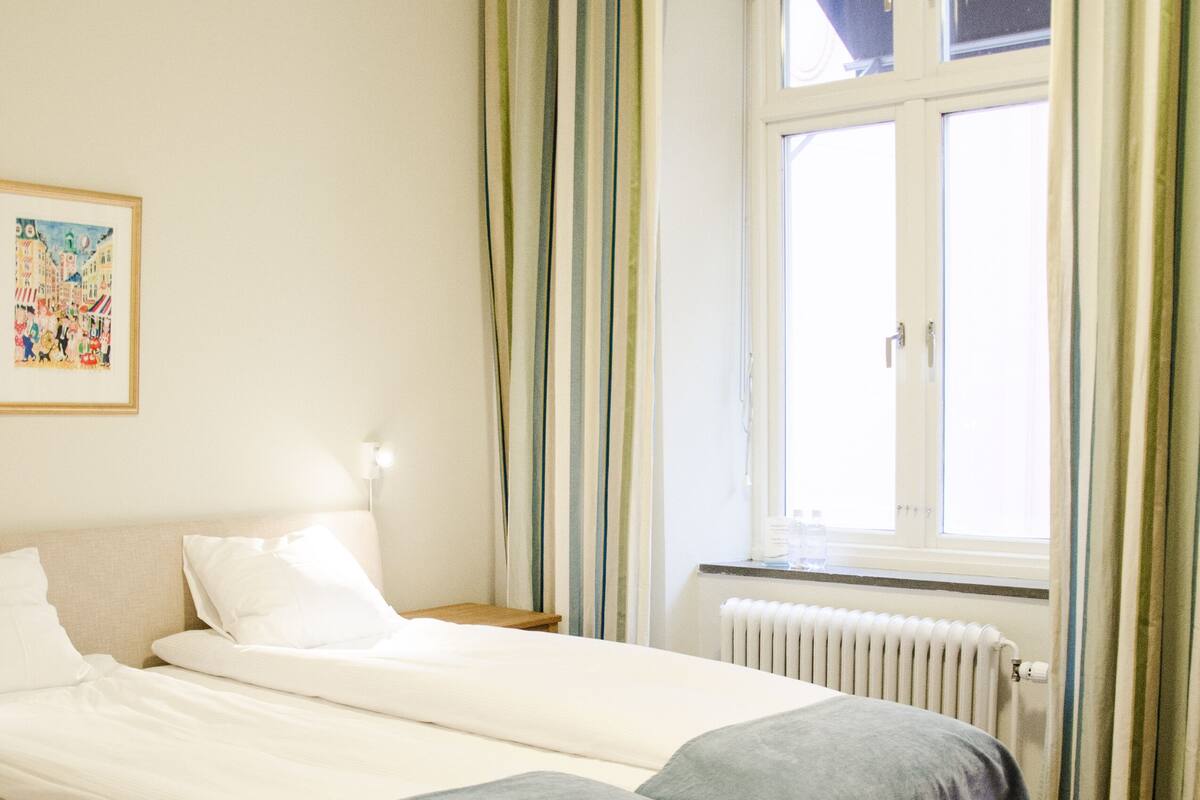A bedroom with two beds, a radiator, and a window with curtains.