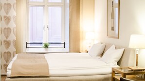 A hotel room with a large bed, a window with curtains, a bedside table with a lamp, and a chair.