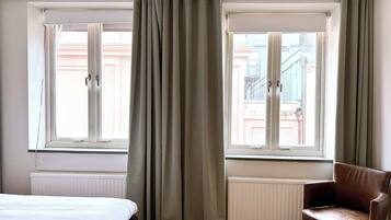 Una habitación de hotel con una cama, una silla, dos ventanas y un radiador.