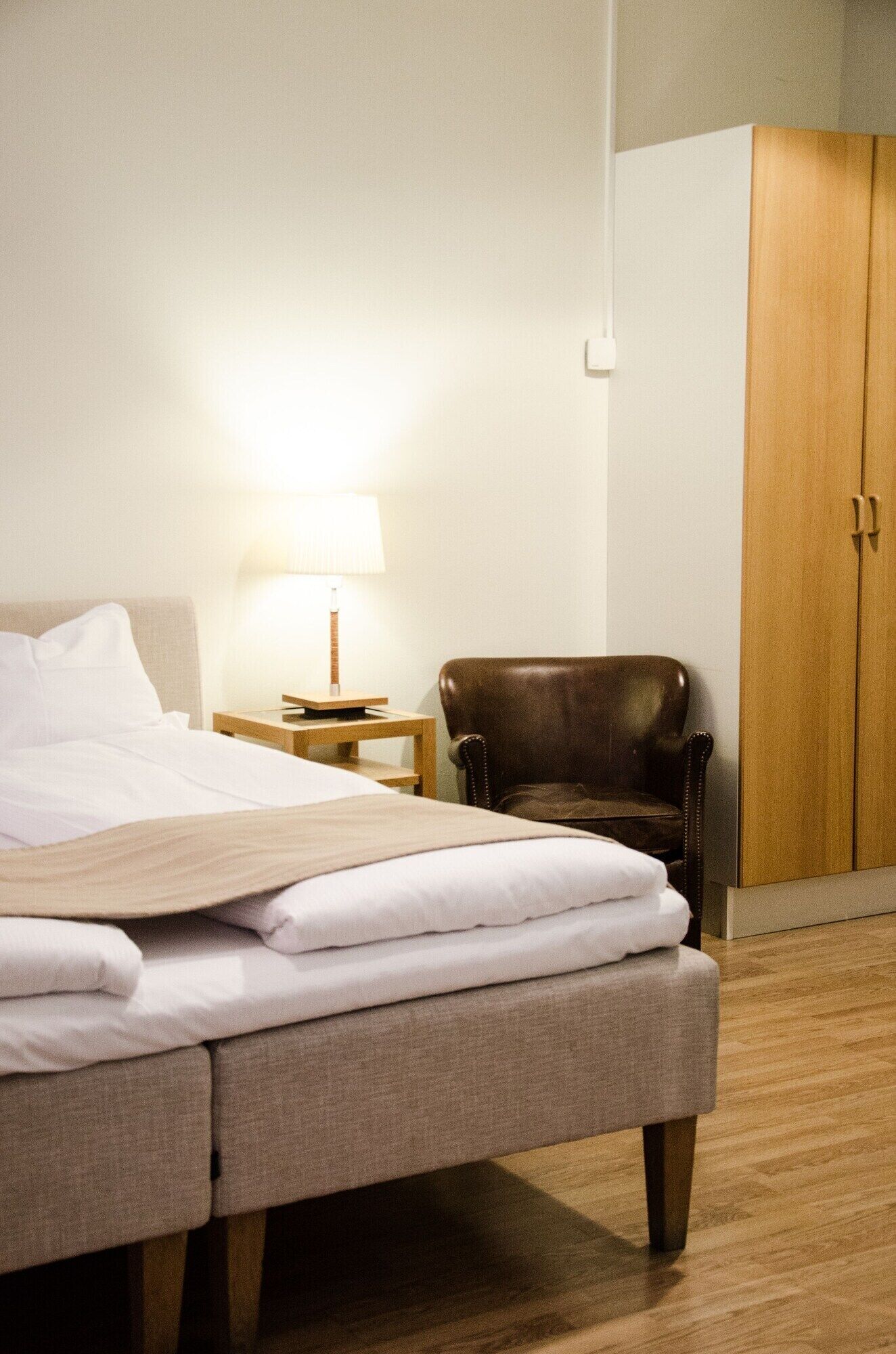 Une chambre d’hôtel comprenant un lit, une chaise, une table de chevet avec une lampe et une armoire.