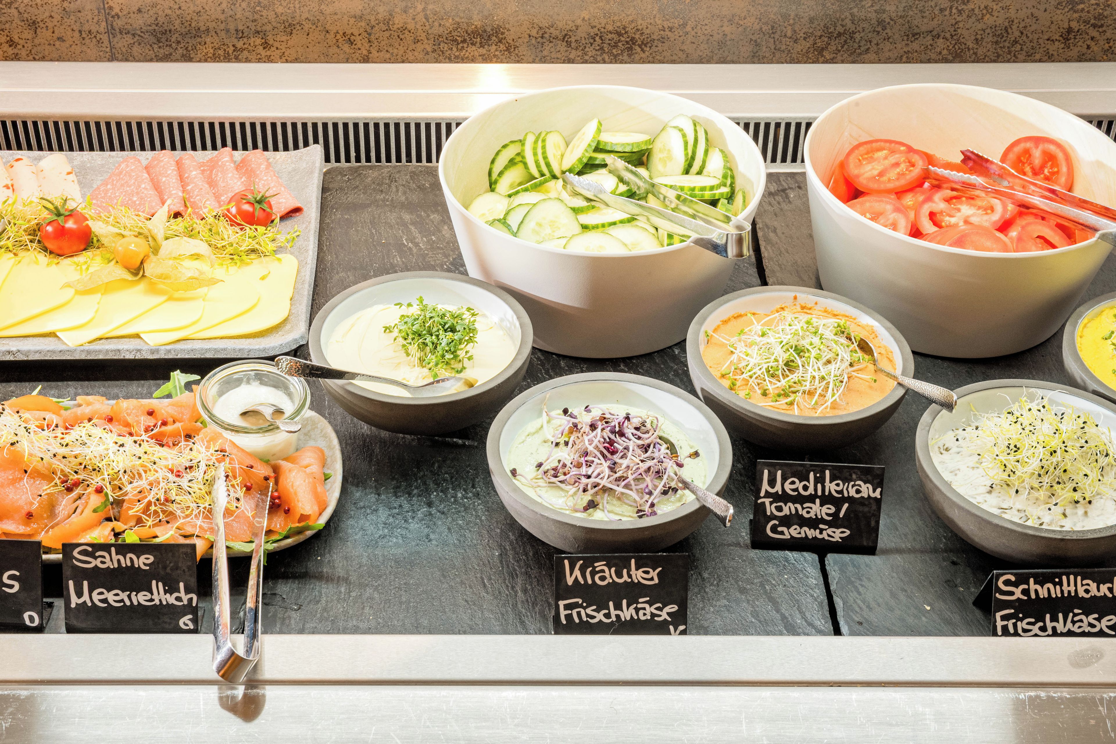 A buffet with various food options including salmon, cucumbers, tomatoes, and different dressings.