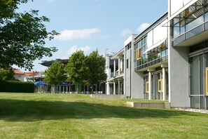 A modern building with a flat roof, large windows, and a grassy courtyard. - GenoHotel Baunatal (Baunatal)