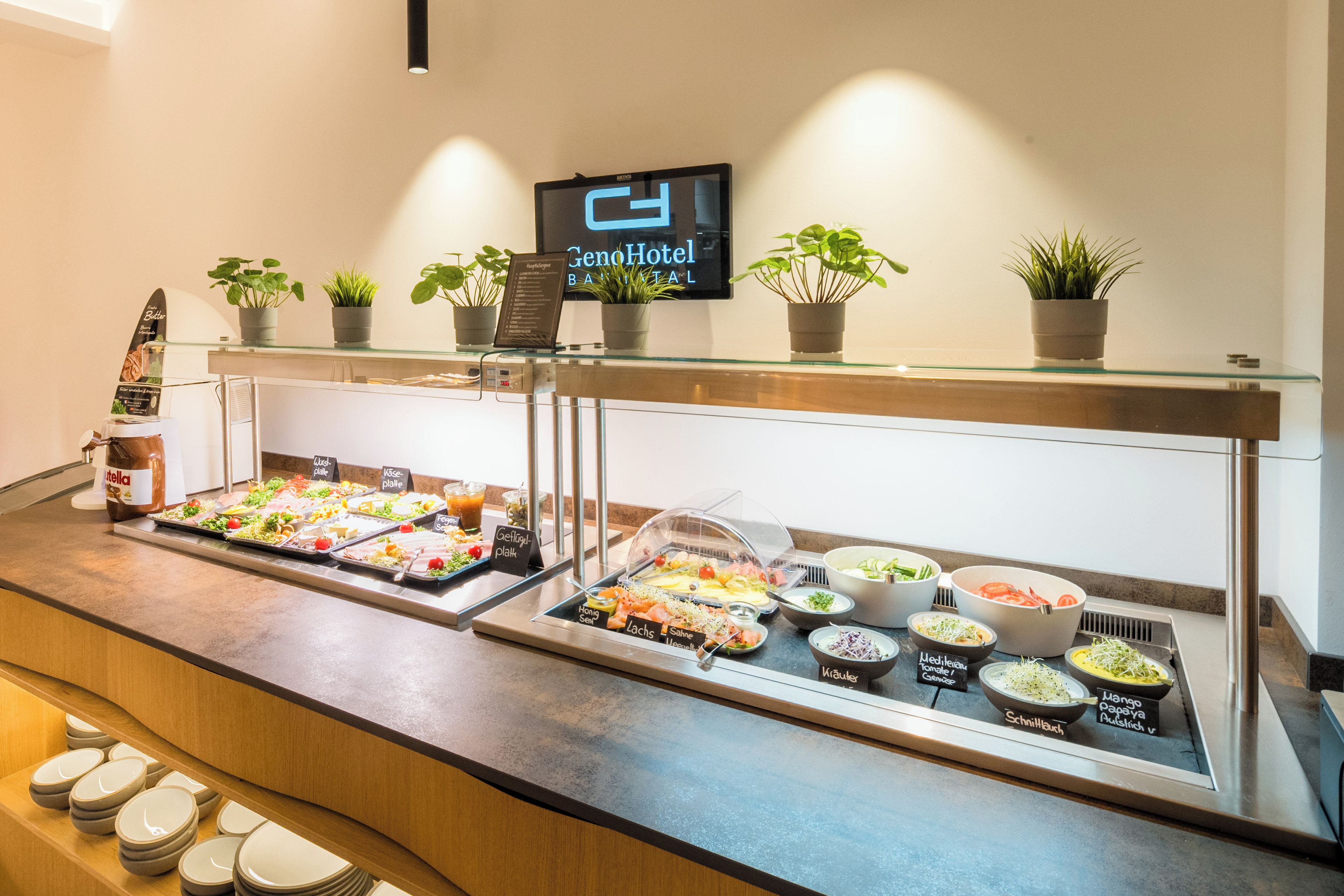 Montaje de buffet con diversas opciones de comida, un reloj digital y plantas en macetas sobre una barra de vidrio.