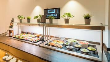 Montaje de buffet con diversas opciones de comida, un reloj digital y plantas en macetas sobre una barra de vidrio.