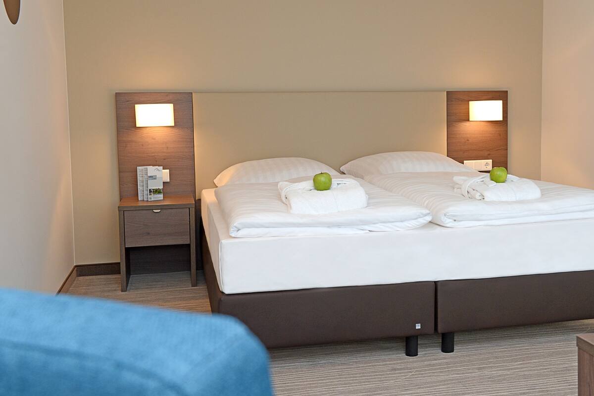 A hotel room with a double bed, two bedside tables, a nightstand, and a wall-mounted light fixture.