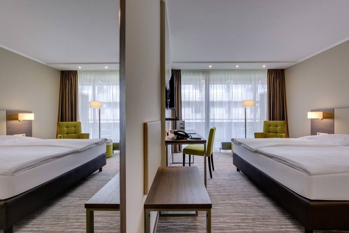 A hotel room with two beds, a desk, a chair, and a TV.