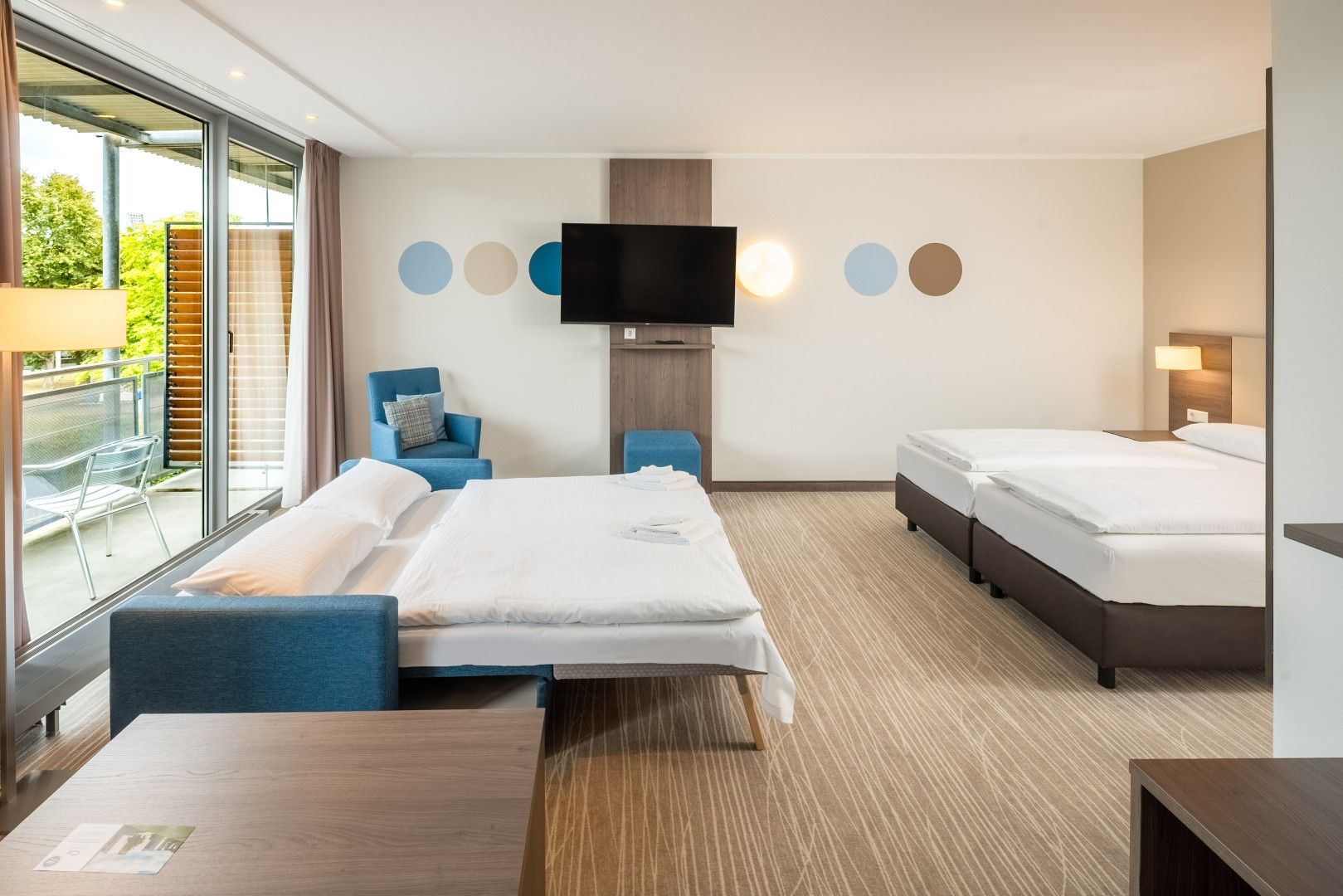 A hotel room with a bed, a sofa, a TV, and a balcony with a view.