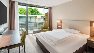 A hotel room with a bed, a desk, a chair, a bedside table, and a view of the outdoors.