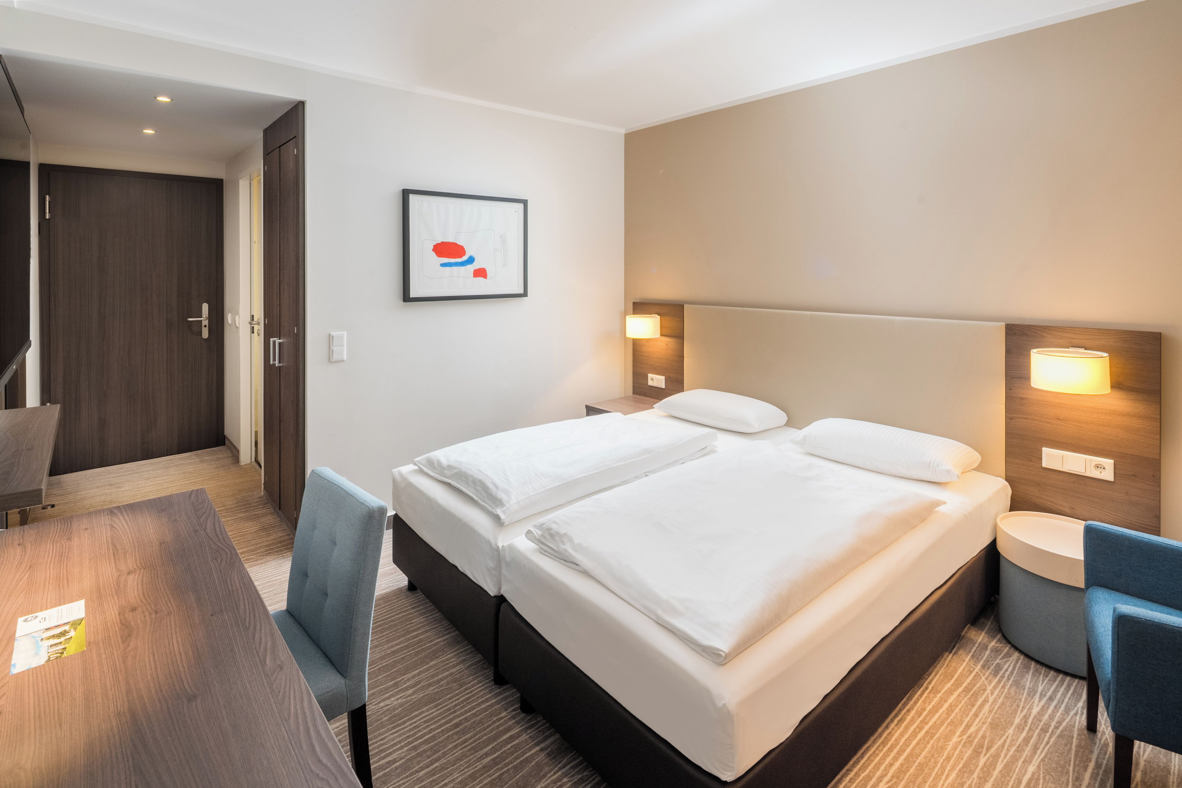 Une chambre d’hôtel avec un lit double, un bureau, une chaise et un tableau encadré au mur.