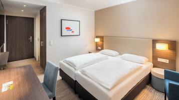 Ein Hotelzimmer mit Doppelbett, Schreibtisch, Stuhl und einem gerahmten Bild an der Wand.