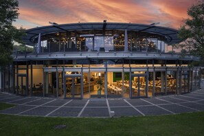 A modern building with a glass facade, multiple levels, and a covered outdoor seating area. - GenoHotel Baunatal (Baunatal)