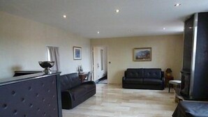 A spacious living room with a black sofa, a fireplace, and a tiled floor. - Hôtel Saint Alban (Saint-Maur-des-Fosses)
