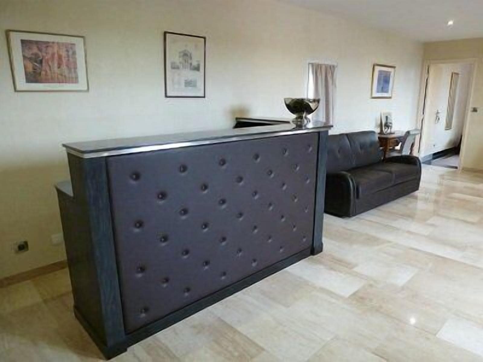 Un salon moderne avec un canapé capitonné de couleur sombre, une table basse en verre et un tableau encadré accroché au mur.