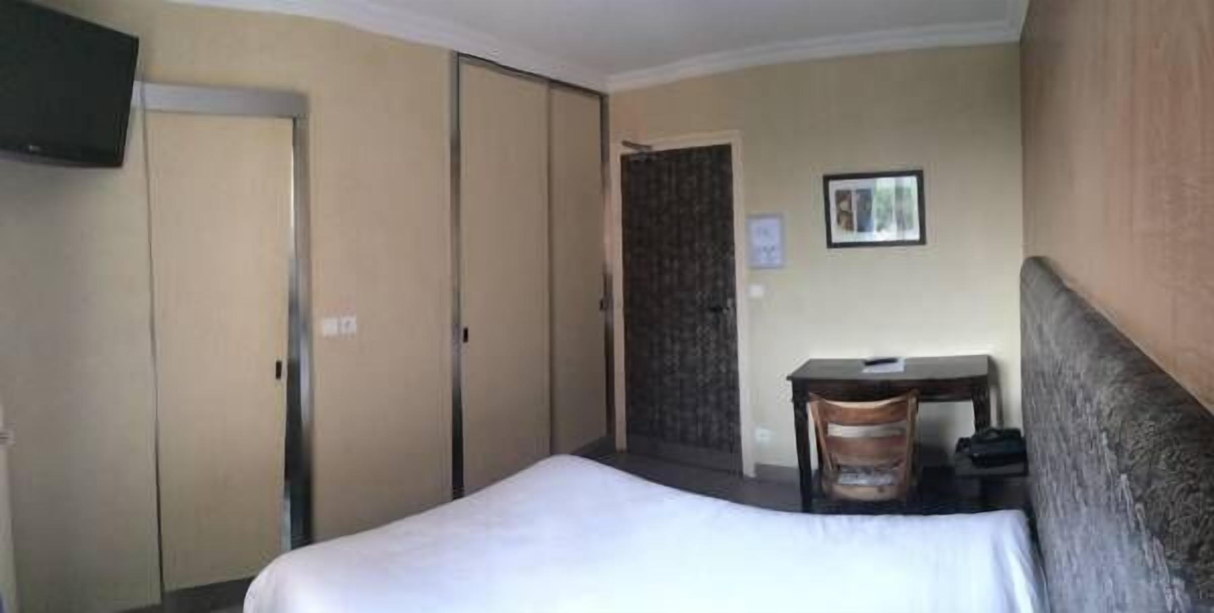 A hotel room with a bed, a desk, a chair, a wardrobe, and a television.