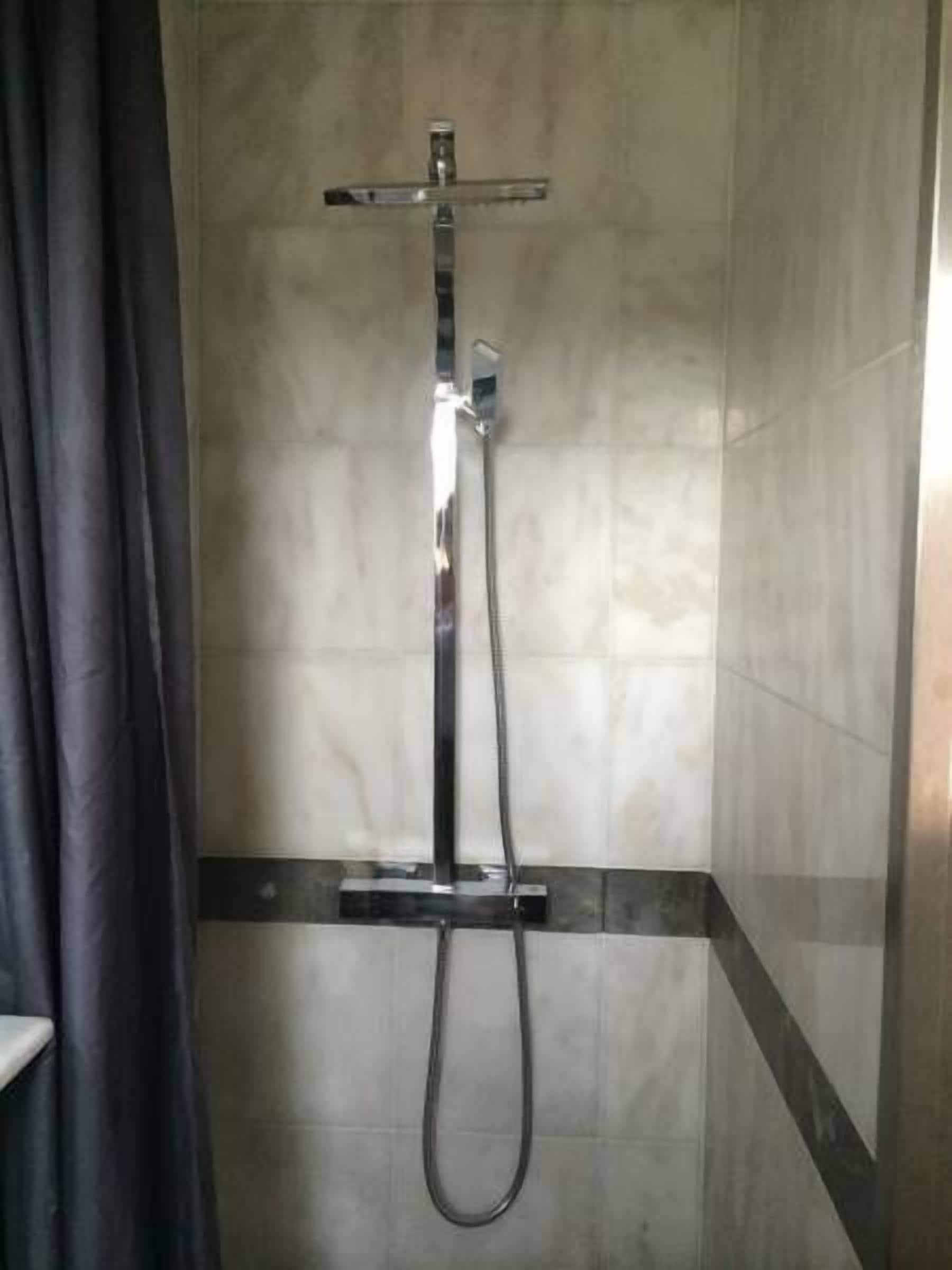 Ducha con cabezal de ducha de mano y cabezal de ducha fijo en el techo, instalada en una pared con salpicadero de azulejos.