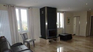 A spacious living room with a black leather sofa, a flat-screen TV, and a fireplace. - Hôtel Saint Alban (Saint-Maur-des-Fosses)