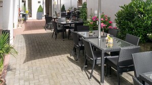 An outdoor patio with tables and chairs, umbrellas, and potted plants. - Hotel Bitburger Hof (Bitburg)