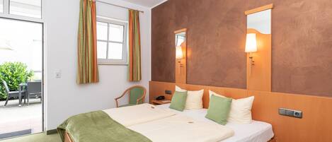 A double bed with green and white bedding, a bedside table with a lamp, a chair, and a window with curtains.