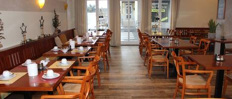 A spacious dining area with multiple wooden tables and chairs, a long counter, and a view of the street through large windows.
