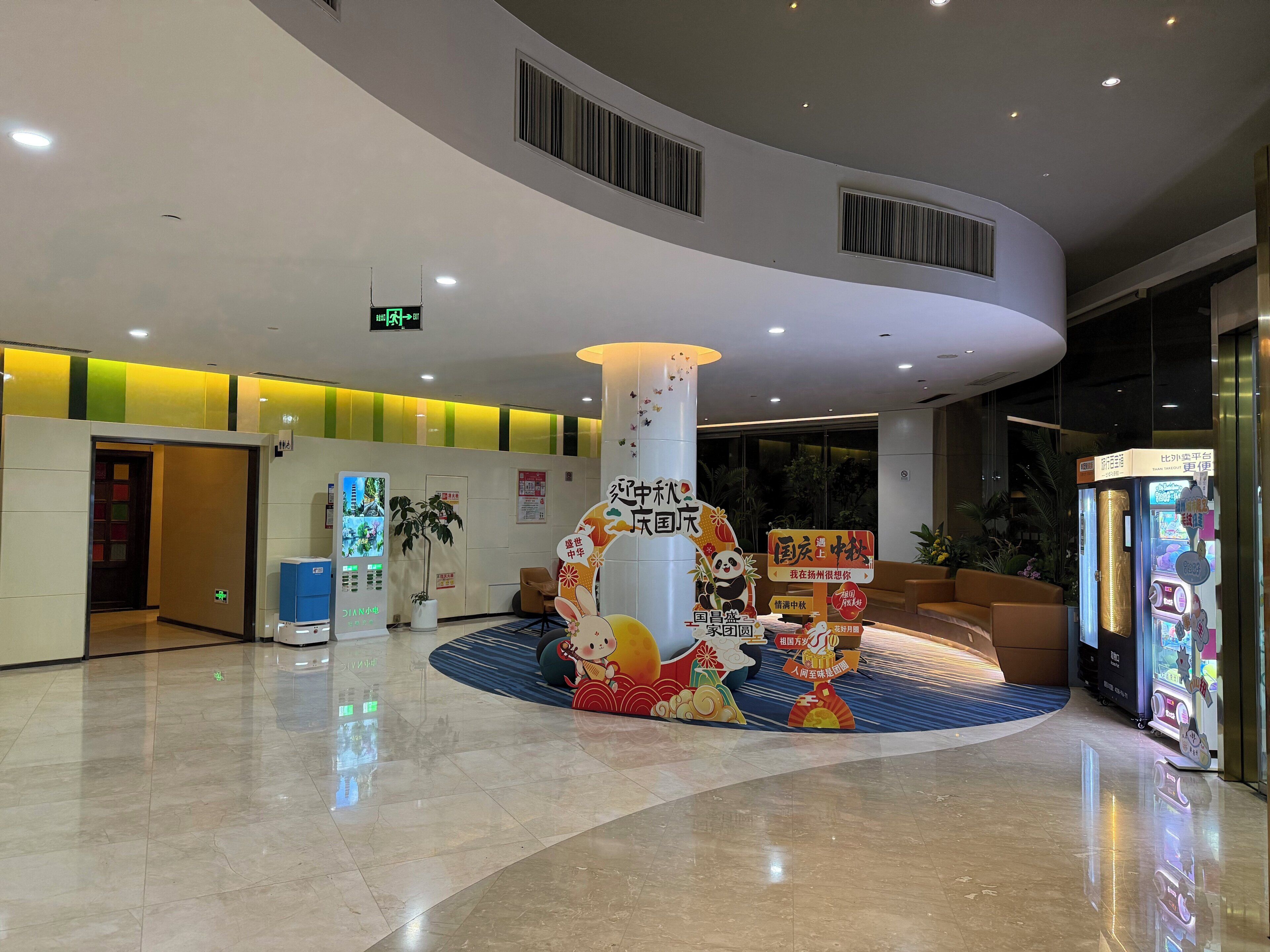 A hotel lobby with a central column, a reception desk, vending machines, and a decorative panda sculpture.