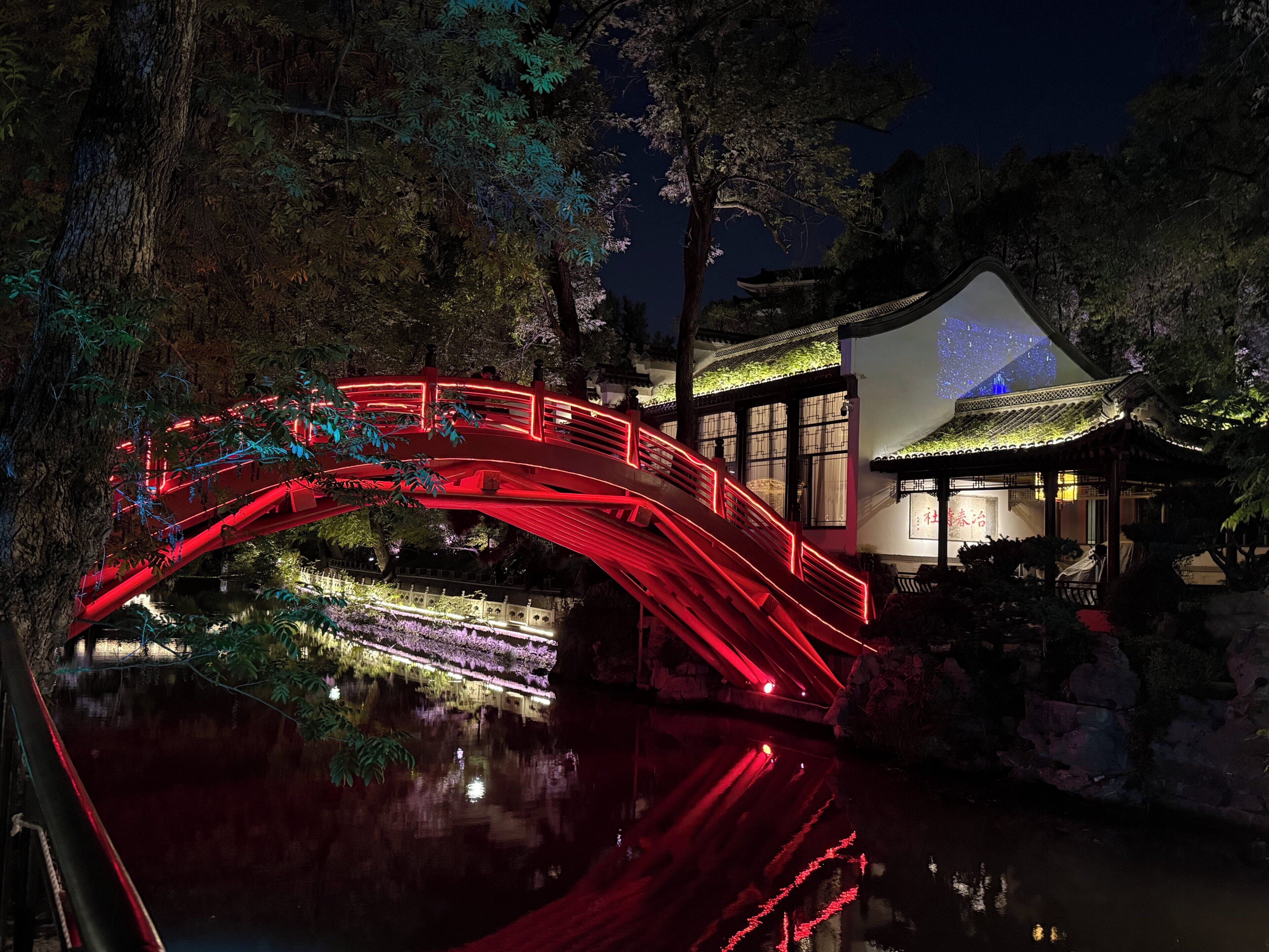 A traditional building with a red-lit bridge over a reflective water body.