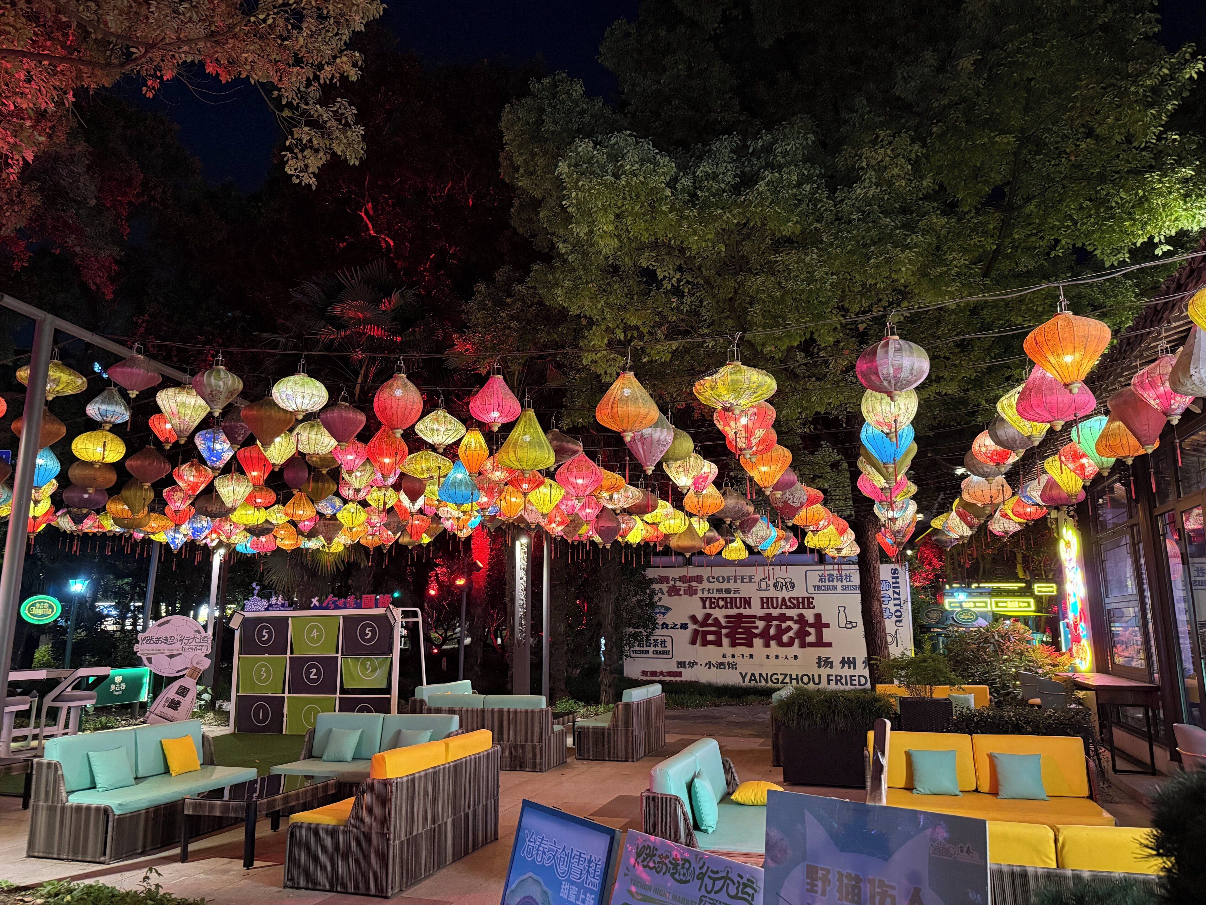 An outdoor seating area with multiple couches and tables, surrounded by colorful hanging lanterns.