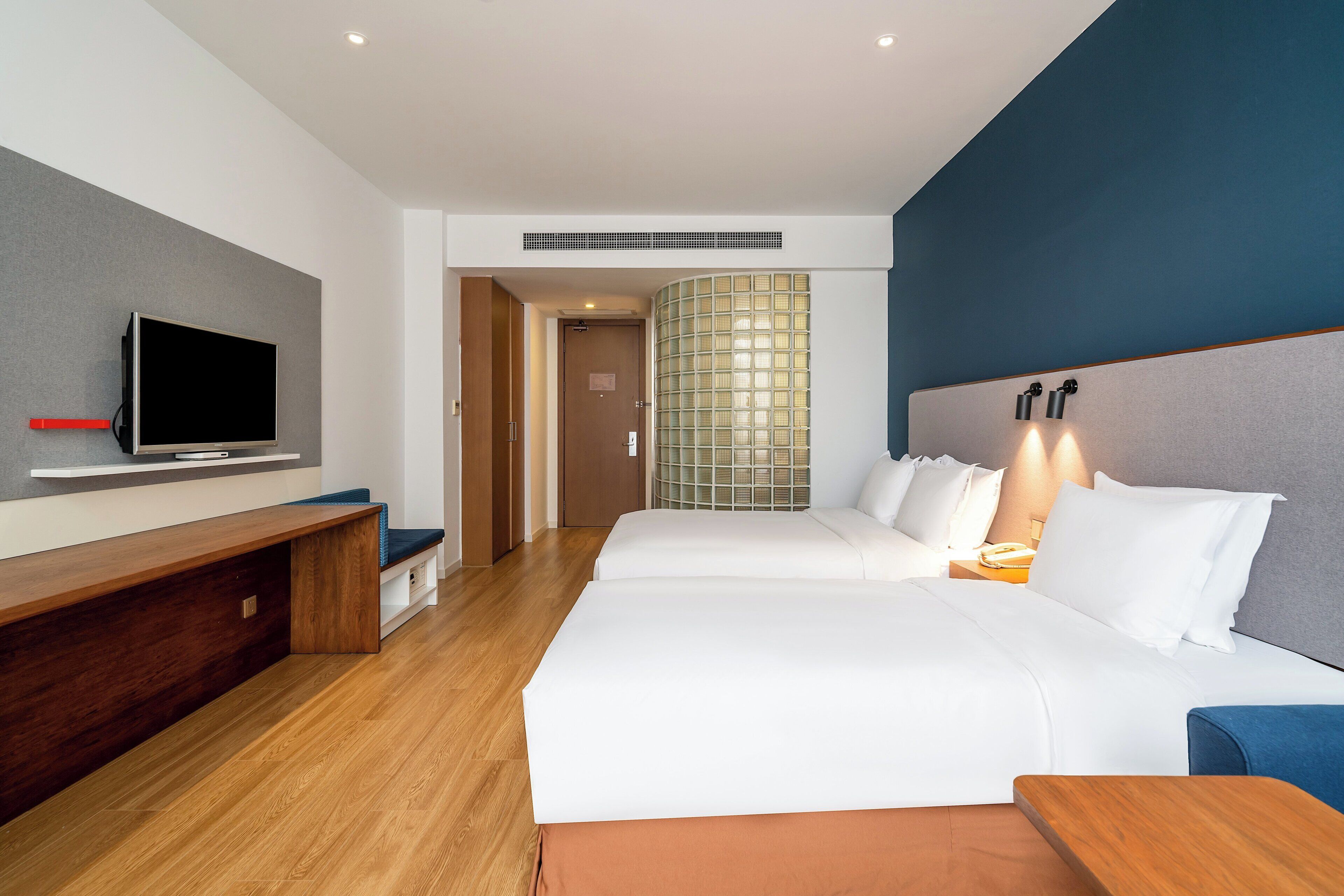 Habitación de hotel con dos camas, televisión, escritorio y un ventanal con vistas.