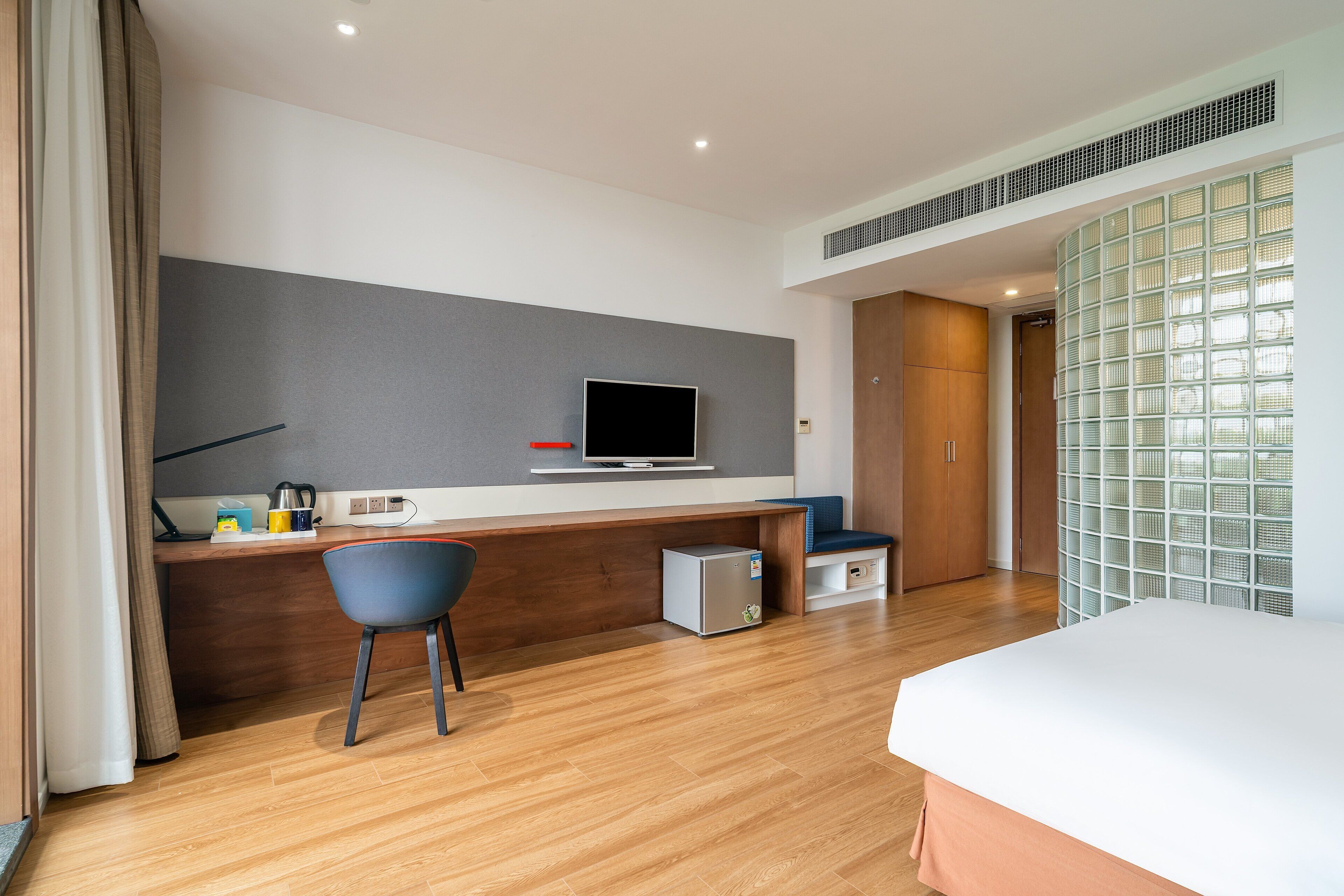 Una habitación de hotel moderna con un escritorio de madera, un televisor, un refrigerador pequeño y una cama.