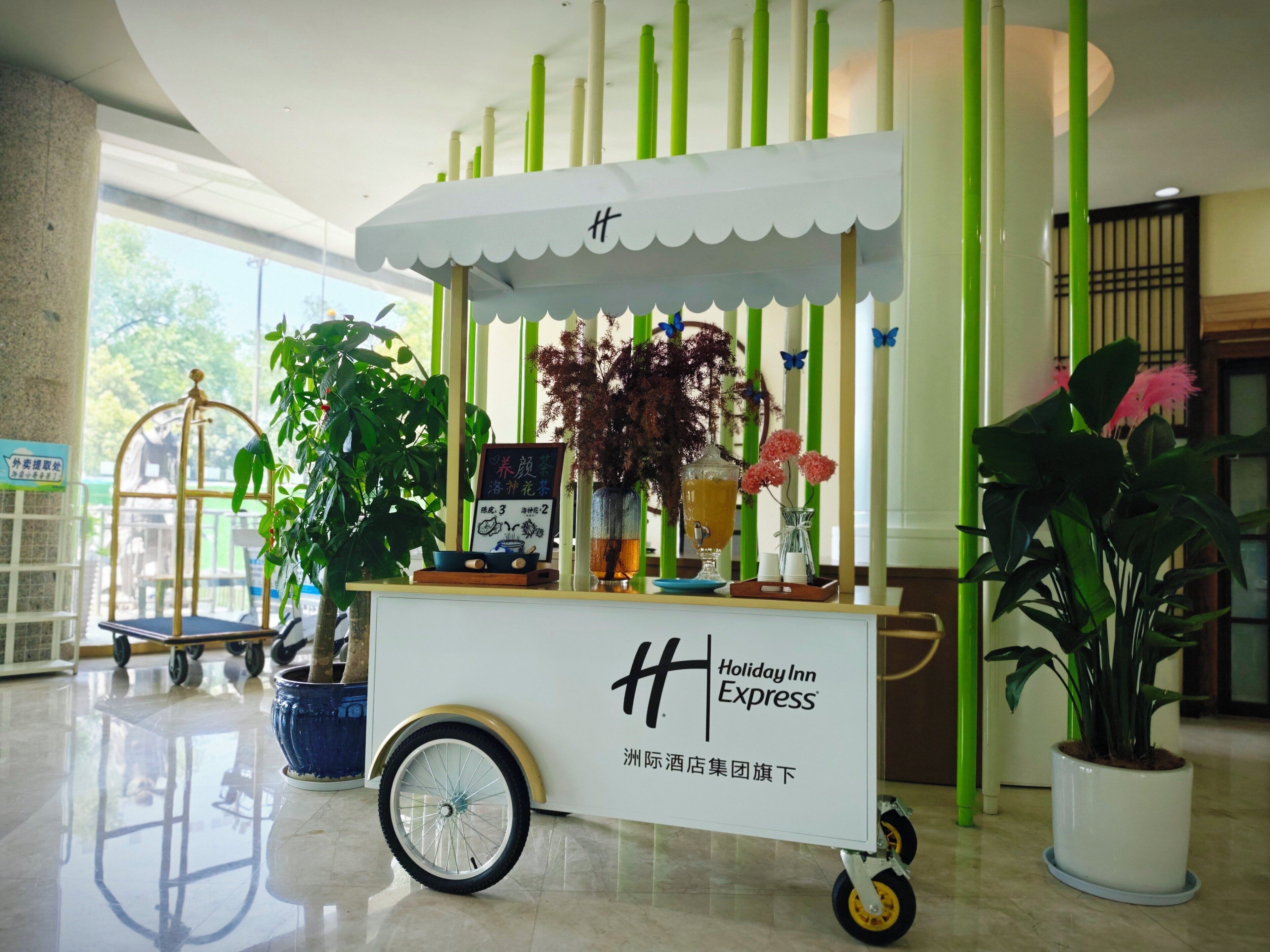 A stationary cart with a sign for Holiday Inn Express, featuring a menu board, a vase with flowers, and a potted plant.