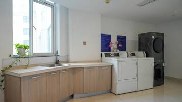 Una cocina moderna con un lavamanos integrado, armarios de madera, encimera blanca, una ventana con una planta y una lavadora y secadora apiladas.