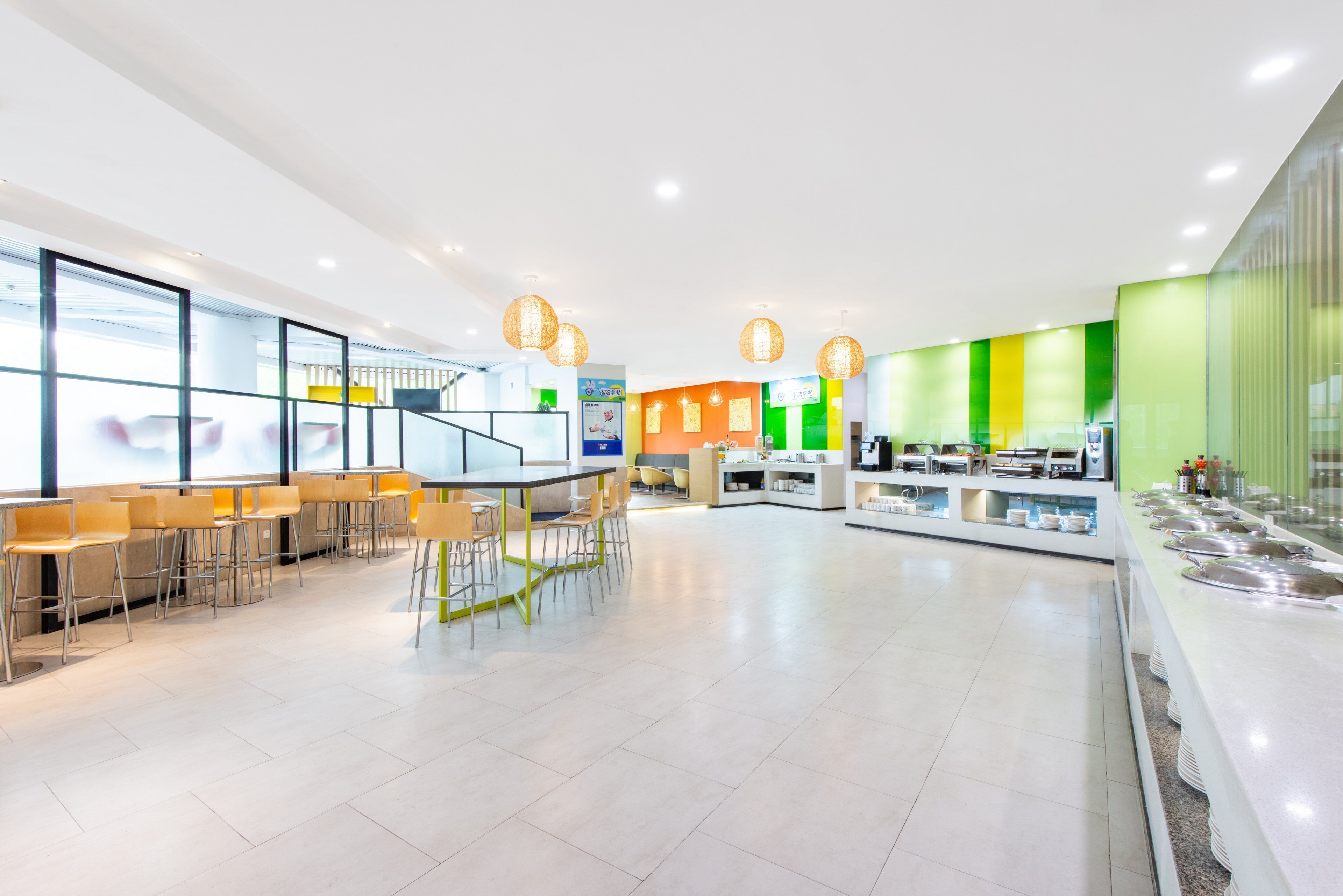 Une cafétéria moderne avec de longues tables et des chaises, un espace buffet et un escalier menant à un niveau supérieur.